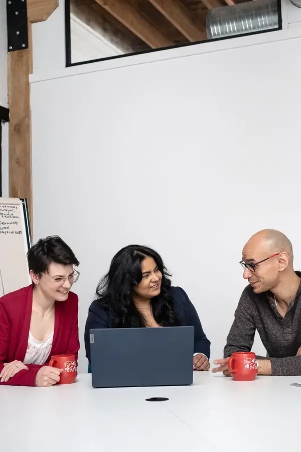 Three individuals collaborating at a table, engrossed in their work on a laptop. GEDI Hub promotes workplace EDI resources and diversity inclusion.